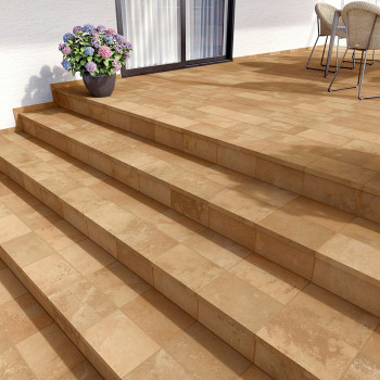 Los rodapies de terracota forman un patio iluminado por el sol con cuatro escalones que conducen hacia arriba. Una planta en maceta y sillas decoran cerca de una ventana.