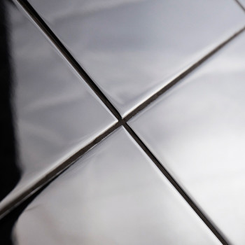 Vier glänzende, metallische Kacheln sind in einem Raster angeordnet und reflektieren Licht und Schatten. Sie bilden sich kreuzen