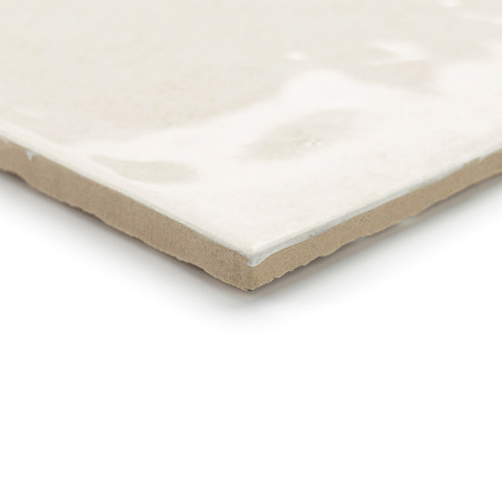 A ceramic tile sits flat, displaying a glossy, smooth, cream-colored surface with subtle variations, and rests against a white b