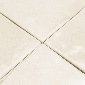 Revestimentos cerâmicos de cor creme dispostos em grade, com leve textura e linhas de rejunte visíveis, criando uma superfície d