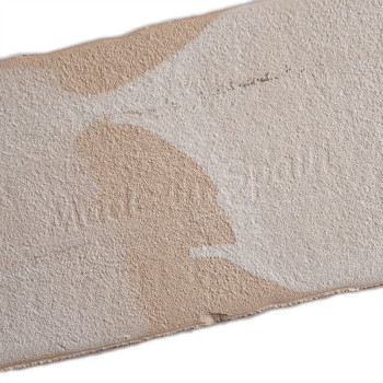 Een rechthoekige, getextureerde beige tegel met onregelmatige witte vlekken. De tekst `Made in Spain` is subtiel in reliëf op he