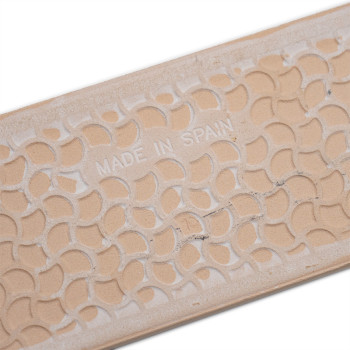 Een beige keramische tegel heeft een herhalend geometrisch patroon en de tekst MADE IN SPAIN in reliëf, rustend tegen een effen 