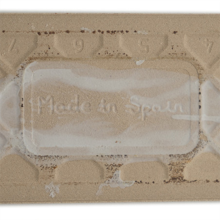 Op een rechthoekige beige tegel staat de tekst `Made in Spain` in reliëf, omringd door een structuurpatroon met de cijfers 9, 5,