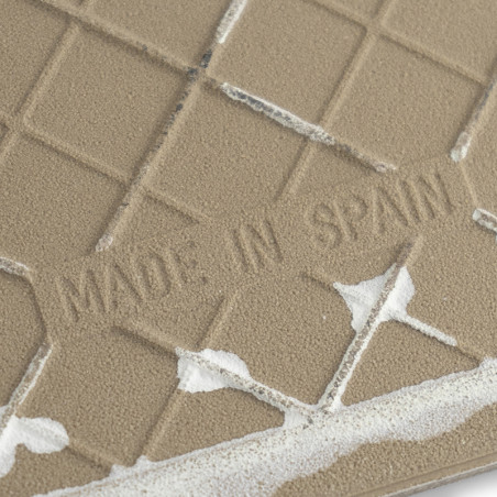 Eine strukturierte Keramikfliese mit dem eingeprägten Text „MADE IN SPAIN“ ist teilweise mit weißem Kleber bedeckt und liegt vor
