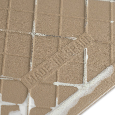 A textured brown tile, embossed with `MADE IN SPAIN,` displays a grid pattern. It is partially covered with white adhesive in a 