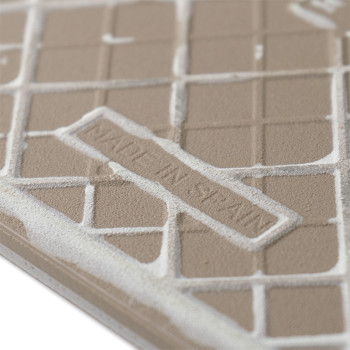 A textured ceramic tile displays a grid pattern embossed with the text `MADE IN SPAIN,` set against a neutral, matte surface.