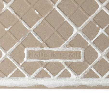 Un azulejo cerámico beige texturizado muestra un patrón de cuadrícula geométrica. El texto `MADE IN SPAIN` está grabado dentro d