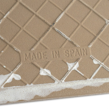 Op een lichtbruine, getextureerde keramische tegel staat de tekst `MADE IN SPAIN` afgebeeld te midden van een rasterpatroon, met