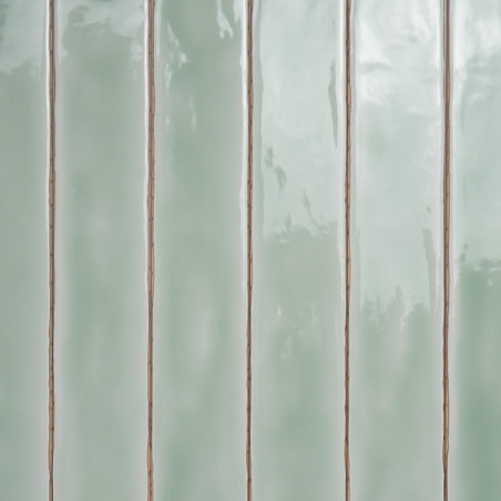Carreaux vert pastel brillants et rectangulaires alignés verticalement. réfléchissant la lumière, créant de légères variations d