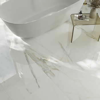 A white marble floor with subtle gray and gold veins reflects light, surrounding a sleek, freestanding bathtub and a glass side 