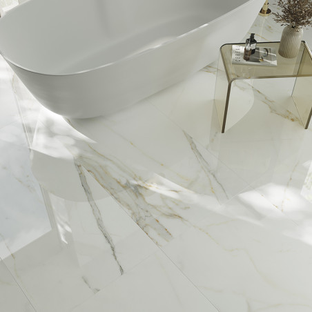 A white marble floor with subtle gray and gold veins reflects light, surrounding a sleek, freestanding bathtub and a glass side 
