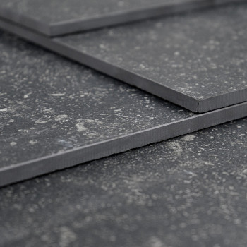 Tres azulejos de color gris oscuro superpuestos, que descansan sobre una superficie texturizada, muestran un patrón moteado con 