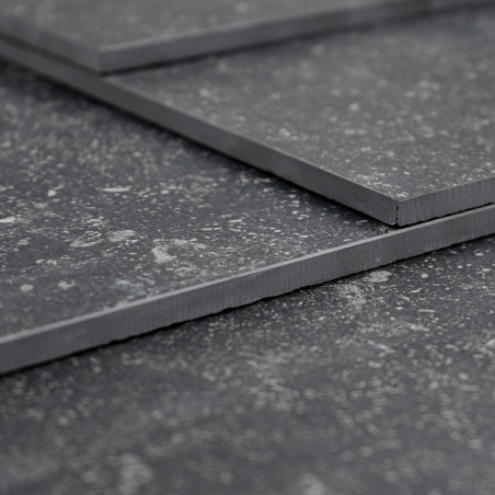 Tres azulejos de color gris oscuro superpuestos, que descansan sobre una superficie texturizada, muestran un patrón moteado con 