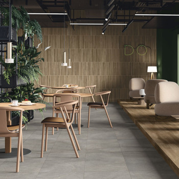 Des tables et des chaises en bois sont posées sur un sol carrelé gris clair dans un café moderne doté de verdure et d'un éclaira
