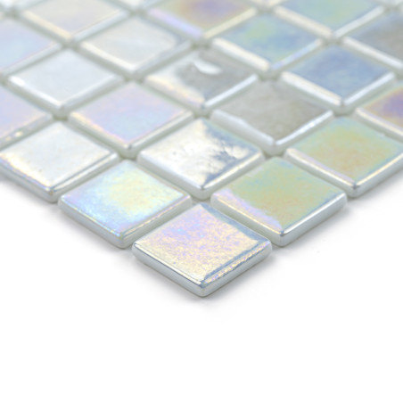 Iridescent glass tiles shimmer, arranged in a grid pattern, creating a reflective, colorful mosaic on a smooth surface.