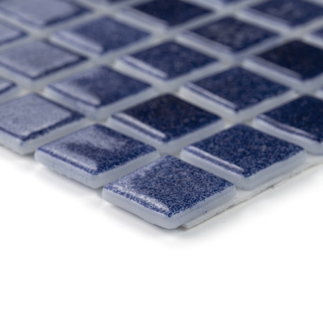 Blue glass tiles laid uniformly, reflecting light, form a sleek mosaic pattern on a flat surface.