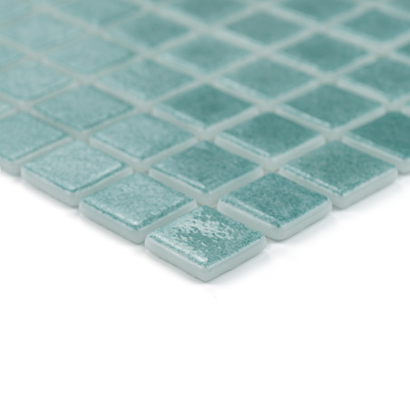Square teal glass tiles arranged in a grid pattern, displaying a shiny, reflective surface, atop a smooth backdrop.
