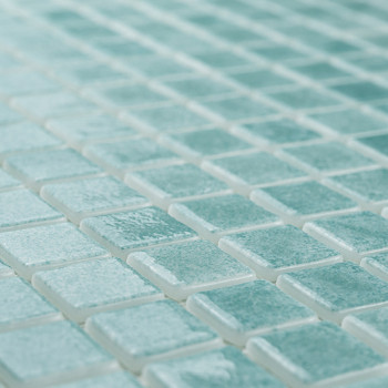 Glass tiles form a mosaic, creating a shimmering pattern on a flat surface, with light enhancing their turquoise hue.