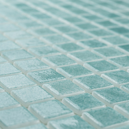 Glass tiles form a mosaic, creating a shimmering pattern on a flat surface, with light enhancing their turquoise hue.
