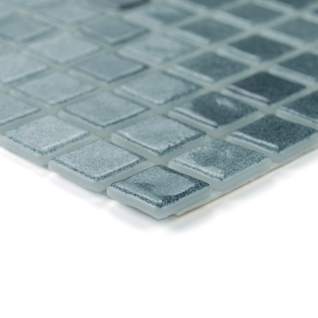 Square glass tiles arranged neatly, reflecting light, create a textured, shimmering surface in muted gray tones.