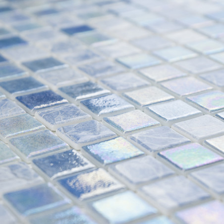 Iridescent glass mosaic tiles glisten on a surface, displaying varying shades of blue and white in a grid pattern.