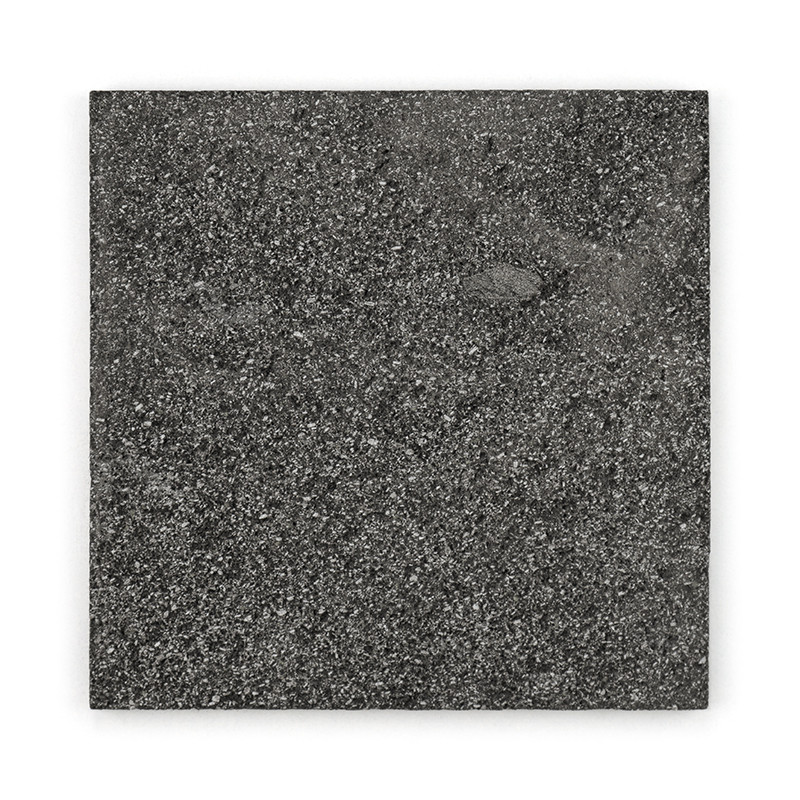 Square stone tile displays speckled, dark gray texture, resting against a plain white background.