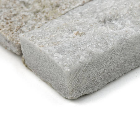 A rough-textured, rectangular stone tile, sitting on a neutral surface, showcases mineral grains and subtle color variations.