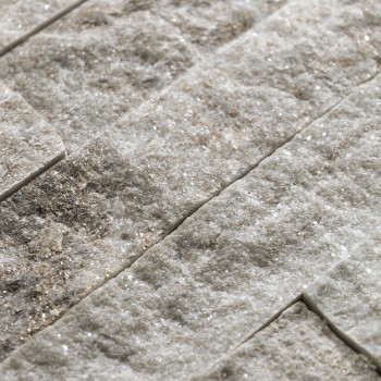 Rough, textured stone tiles lie stacked horizontally, showcasing a natural, earthy blend of light and dark tones.