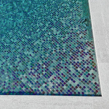 Blue and green mosaic tiles create an intricate pattern, lining the bottom of a rectangular swimming pool.