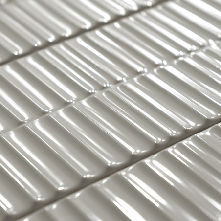 Carreaux de céramique rectangulaires disposés selon une grille uniforme, réfléchissant la lumière et projetant des ombres douces