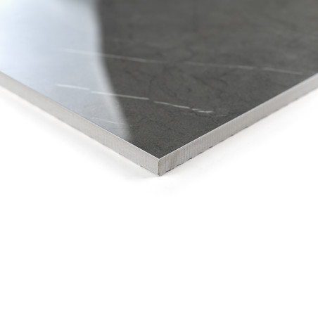 A polished, dark gray tile with subtle vein patterns rests on a white surface, reflecting soft light in a minimalist setting.
