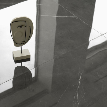Uma cabeça escultural em um suporte projeta uma sombra sobre azulejos cinza lisos e reflexivos, sugerindo um espaço moderno e mi