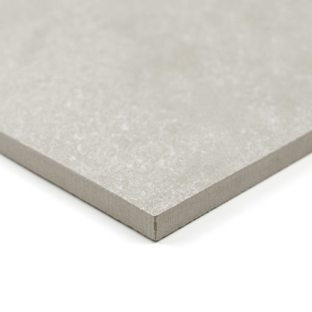 Un azulejo cuadrado de color gris claro con una textura suave descansa sobre un fondo blanco, mostrando sus bordes finos y recto