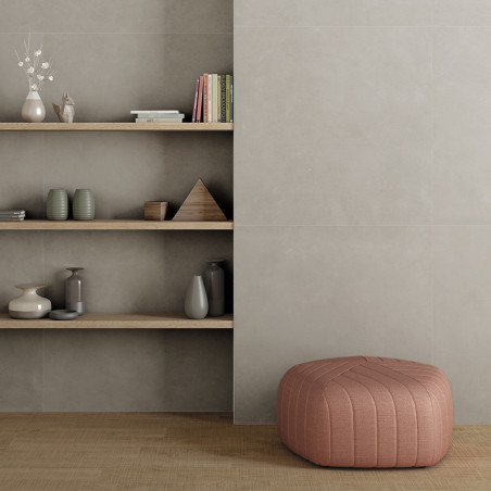 Una otomana rosa descansa sobre un piso de madera junto a estantes empotrados minimalistas que sostienen jarrones, libros y pequ