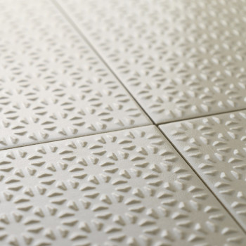 Los azulejos cerámicos texturizadas forman un patrón repetido de formas de rayos de sol en un suave color beige, dispuestas cuid