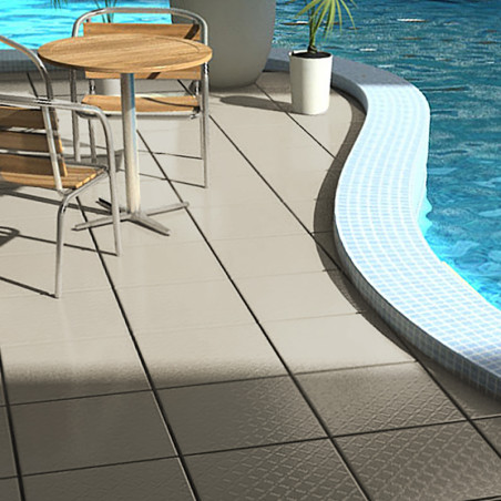 Uma mesa redonda de madeira com cadeiras de metal fica sobre azulejos bege ao lado de uma piscina curva, refletindo a luz do sol