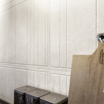 Una pared de textura clara presenta líneas verticales y horizontales, con latas de metal debajo y una tabla de cortar de madera 