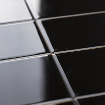 Shiny black ceramic tiles are arranged in a grid pattern, reflecting light softly, set within narrow grout lines.
