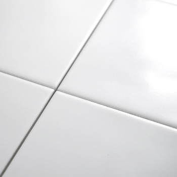 Quatre carreaux de céramique blancs brillants se croisent, formant un motif de grille sur une surface lisse, réfléchissant la lu