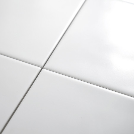 Quatre carreaux de céramique blancs brillants se croisent, formant un motif de grille sur une surface lisse, réfléchissant la lu