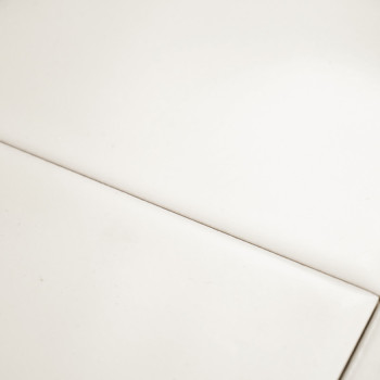 Un carreau blanc lisse et brillant repose à plat, coupé par une fine ligne de coulis droite, créant un motif géométrique minimal