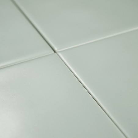 Cuatro azulejos de color verde claro se unen en las esquinas formando una cuadrícula, creando una superficie lisa y limpia con s