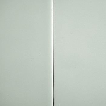 Un azulejo gris claro brillante con una costura vertical divide la superficie, sobre un fondo liso.