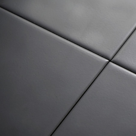 Quatre carreaux de céramique lisses gris foncé sont alignés selon un motif de grille, formant une surface moderne et homogène av