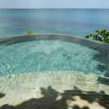 Clear water ripples over stone tiles in an infinity pool, seamlessly blending into the vast ocean horizon.