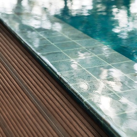 A grid of turquoise stone tiles borders a reflective swimming pool beside a textured wooden deck.