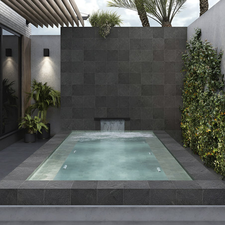 Dark stone tiles form a water feature wall, with water cascading into a small, rectangular pool. surrounded by lush greenery.