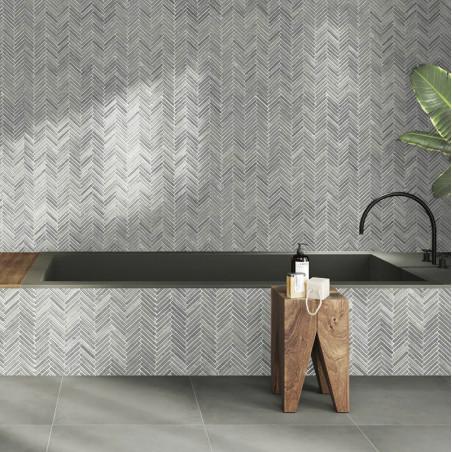 Gray stone tiles form a herringbone pattern wall above a bathtub, complemented by wood stools and a plant.