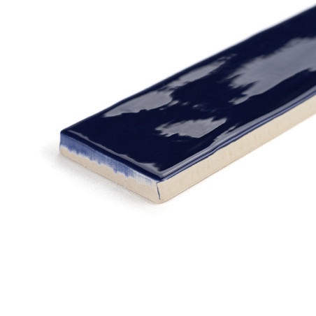 Un azulejo cerámico rectangular muestra un esmalte azul oscuro brillante en la parte superior, con bordes sin vidriar que revela