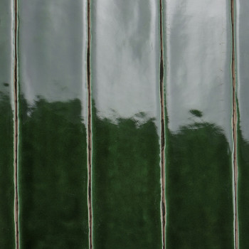 Les carreaux de céramique vert brillant se dressent verticalement et reflètent la lumière. L'alternance de nuances claires et fo